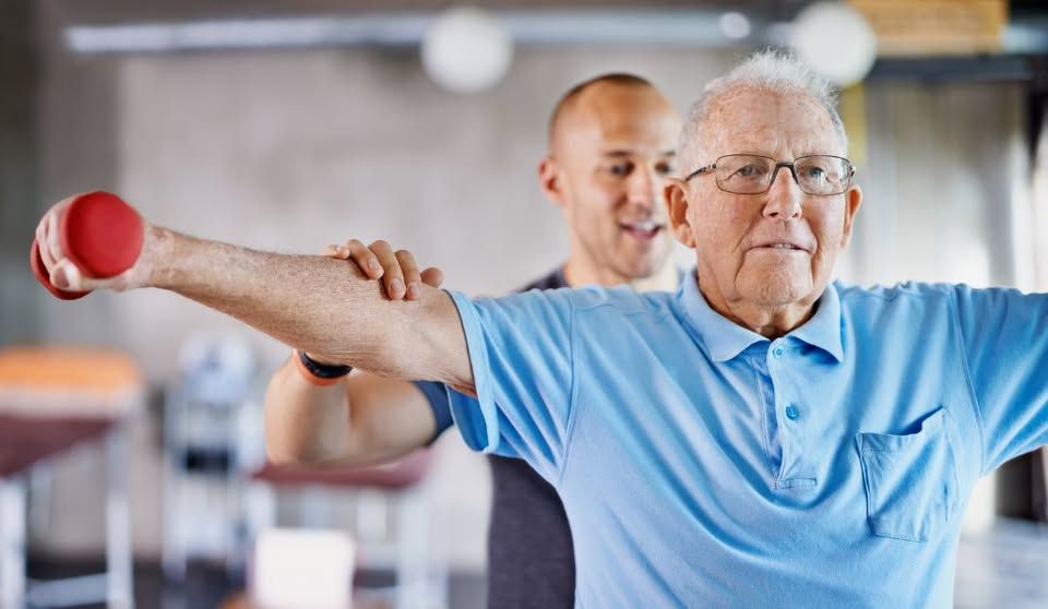 A physiotherapist supporting a patient through gentle exercise at home